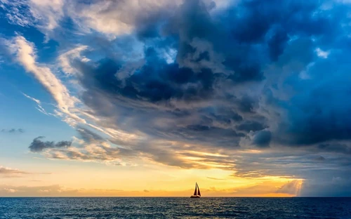 Storm clouds looming over a sailboat at sea.