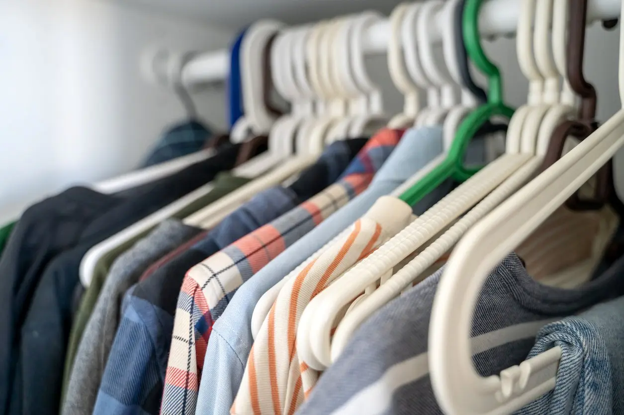 A row of various shirts and pants hanging on plastic hangers inside a closet.
