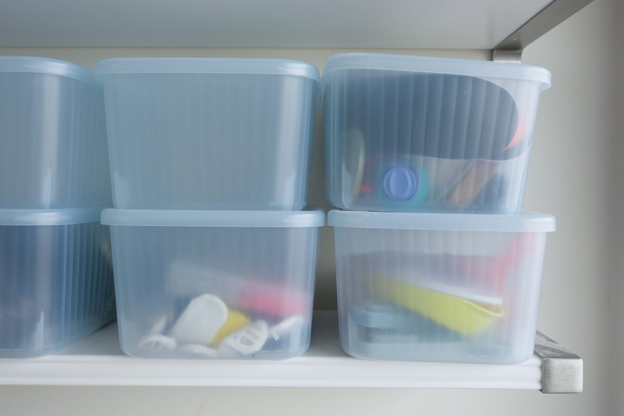Clear plastic storage totes on a shelf and off the ground. 